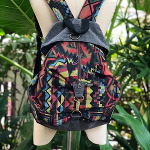 May include: A black backpack with a colourful geometric pattern. The backpack has a zipper closure and a grey fabric flap with a metal ring.