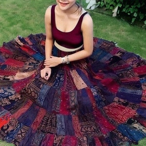Può includere: Una donna indossa una canotta color borgogna e una lunga gonna a patchwork colorata. La gonna è realizzata con diversi tessuti e motivi, e ha uno stile fluido e bohémien.