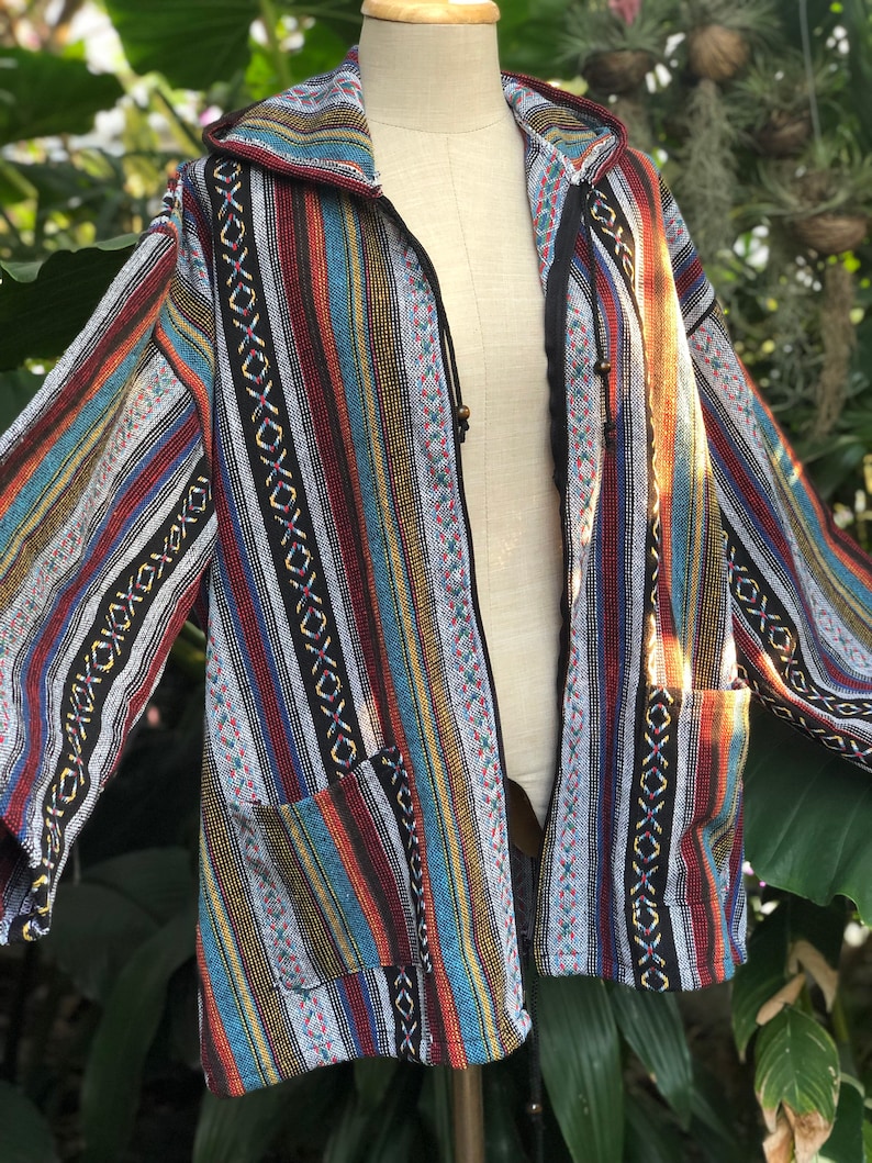 K&ouml;nnte beinhalten: Eine bunt gestreifte Jacke mit Kapuze und zwei Vordertaschen. Die Jacke hat vertikale Streifen in verschiedenen Farben, darunter Rot, Blau, Gelb und Schwarz. Die Jacke wird auf einer Schaufensterpuppe pr&auml;sentiert.