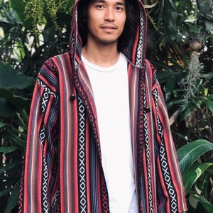 Puede incluir: Chaqueta con capucha a rayas en rojo, negro y blanco. La chaqueta tiene un cordón y se lleva sobre una camiseta blanca. El diseño incluye patrones geométricos y 'XOXO'.