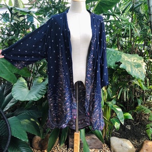 May include: A navy blue kimono with a peacock feather pattern and white polka dots. The kimono is on a wooden mannequin and has a long, flowing silhouette.