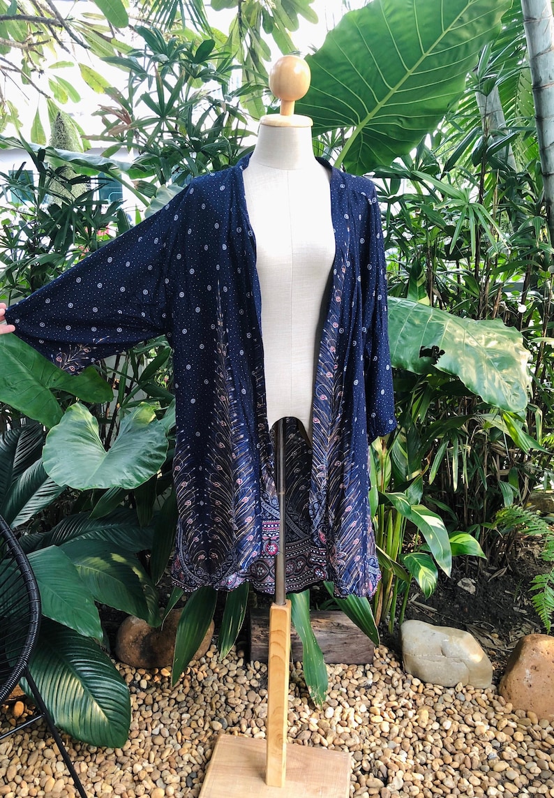 May include: A navy blue kimono with a peacock feather pattern and white polka dots. The kimono is on a wooden mannequin and has a long, flowing silhouette.