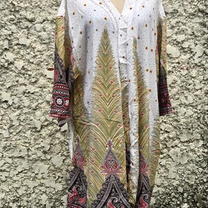 May include: White long-sleeved tunic with a paisley print in shades of green, red, and black. The tunic has a V-neck and a button closure.