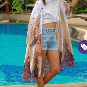 May include: A white and gold patterned kimono with a peacock design. The kimono is worn over a white t-shirt and blue denim shorts.