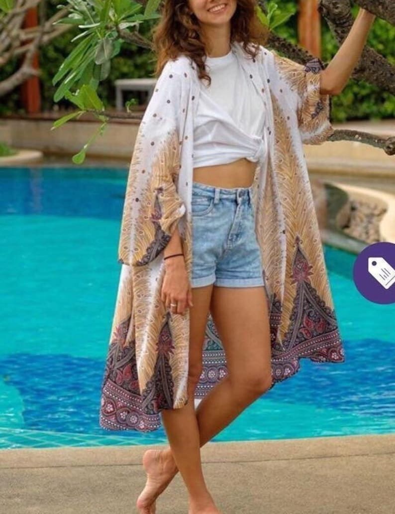 May include: A white and gold patterned kimono with a peacock design. The kimono is worn over a white t-shirt and blue denim shorts.