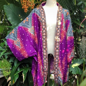 Op de afbeelding: Paarse kimono met een pauwenveerontwerp en oranje en zwarte bies. De kimono is gemaakt van een lichtgewicht stof en heeft een ontspannen pasvorm.