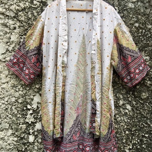 May include: White kimono with a peacock design and red, black and gold trim. The kimono has a white background with small white dots and a large peacock design in the centre. The trim is a red, black and gold paisley pattern.