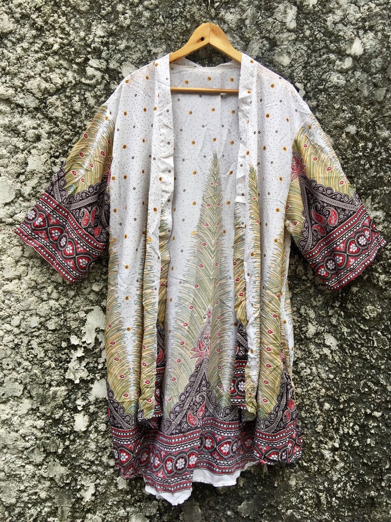 May include: White kimono with a peacock design and red, black and gold trim. The kimono has a white background with small white dots and a large peacock design in the centre. The trim is a red, black and gold paisley pattern.