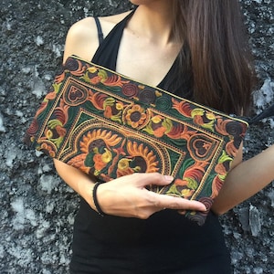 Könnte beinhalten: Eine schwarze Clutch mit bunter Blumenstickerei. Die Stickerei zeigt eine Vielzahl von Farben, darunter Orange, Gelb, Grün und Braun.