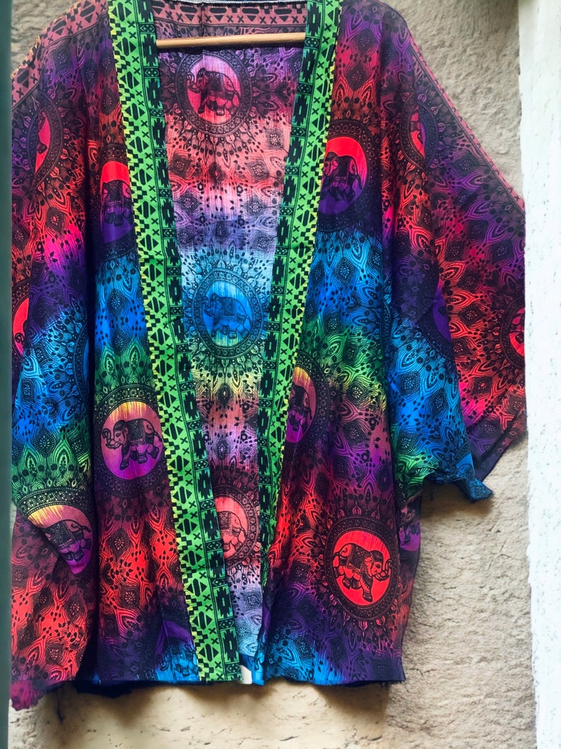 Peut inclure: Un kimono color&eacute; avec un motif ombr&eacute; arc-en-ciel et un imprim&eacute; d'&eacute;l&eacute;phant noir. Le kimono a une bordure verte et noire.