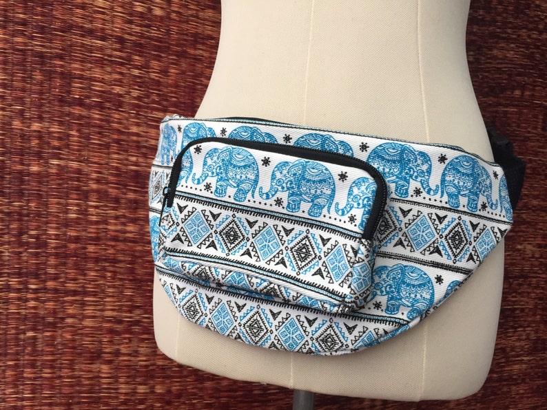 May include: White fanny pack with a blue and black elephant print. The pack has a small zippered pocket on the front.
