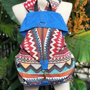 May include: A blue and multi-coloured patterned backpack with a blue flap and a zipper closure. The backpack has a geometric design with red, white, brown, and turquoise accents.