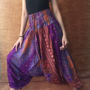 May include: Purple harem pants with a vibrant peacock feather design and a gathered waist. The pants have a wide, loose fit and are made of a lightweight fabric. The pants are paired with a black tank top.
