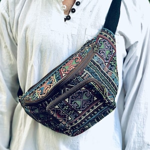 Puede incluir: Riñonera colorida con un patrón geométrico en tonos azules, verdes, rojos y marrones. La bolsa tiene dos compartimentos con cremallera y una correa negra ajustable. La riñonera se lleva cruzada.