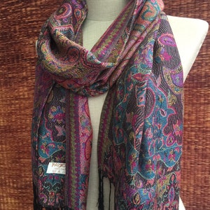 May include: A long, black, fringed scarf with a paisley pattern in shades of pink, blue, and gold. The scarf has a label that reads "Passig 100% Cashmere".