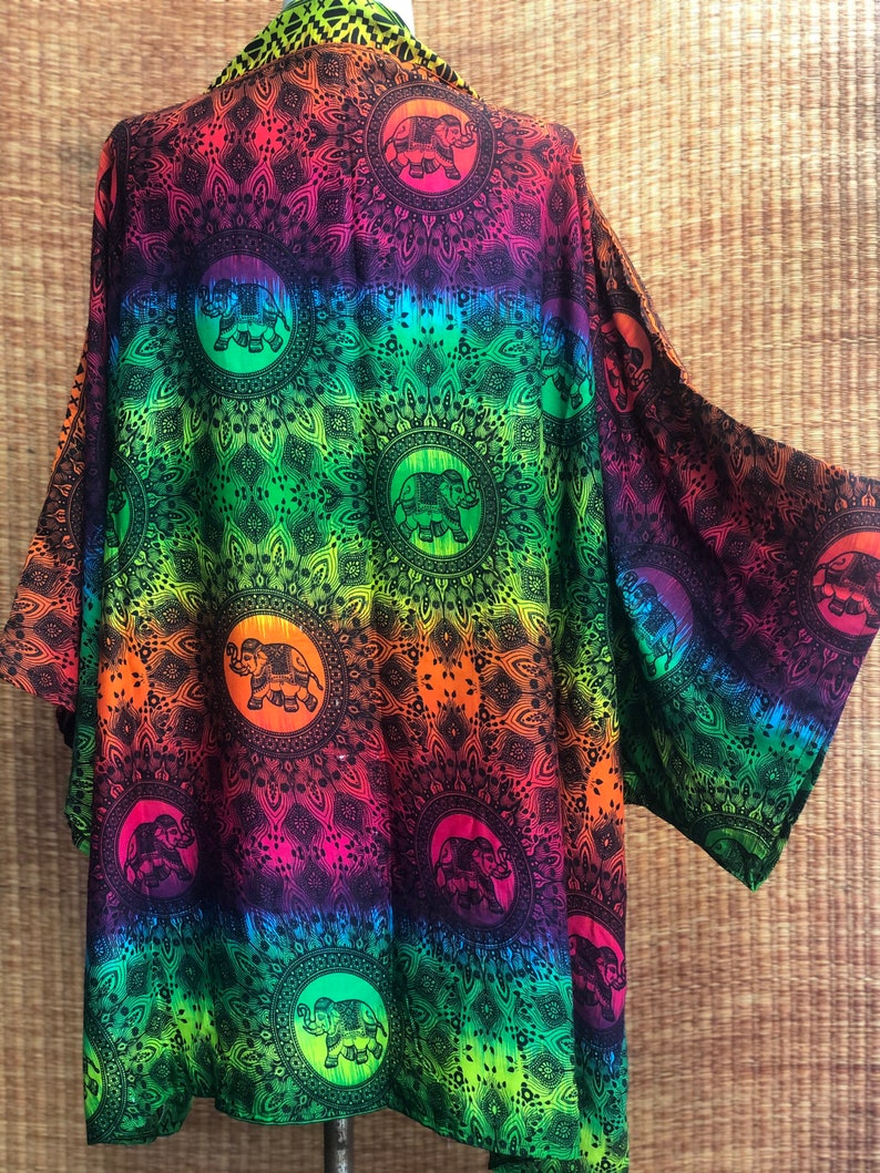 Peut inclure: Un kimono en ombr&eacute; arc-en-ciel avec un motif de mandala noir et des silhouettes d'&eacute;l&eacute;phants. Le kimono a une coupe ample et est fait d'un tissu l&eacute;ger.