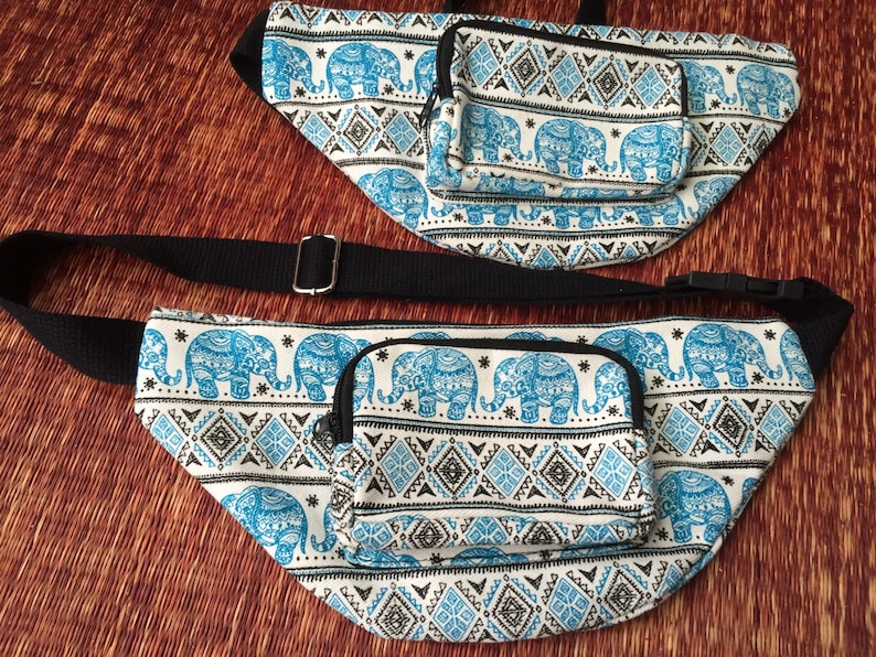 May include: Two fanny packs with blue and white elephant print and black trim. The larger fanny pack has a black adjustable strap. Both fanny packs have a small zippered pocket on the front.