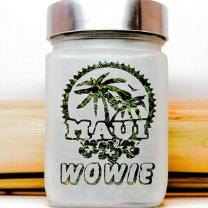 Puede incluir: Tarro de vidrio blanco esmerilado con tapa plateada. El tarro tiene un dise&ntilde;o verde y blanco con una palmera y las palabras "Maui Wowie" impresas en &eacute;l.