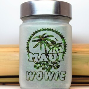 Puede incluir: Un tarro de vidrio esmerilado con tapa plateada. El tarro tiene un dise&ntilde;o verde con palmeras y las palabras "Maui Wowie" en &eacute;l.