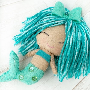 May include: A handmade felt mermaid doll with turquoise hair, a turquoise and white striped bodice, and a turquoise tail with silver glitter accents.