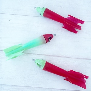 May include: Three toy rockets, one green and two red, with a white background.