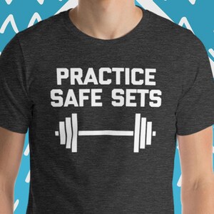 Könnte beinhalten: Ein dunkel-melierter grauer T-Shirt mit dem Text "PRACTICE SAFE SETS" in Weiß, mit einer weißen Hantelgrafik unter dem Text.