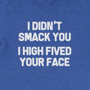 May include: A blue t-shirt with the text "I DIDN'T SMACK YOU I HIGH FIVED YOUR FACE" in white block letters. The shirt is made of a soft material and has short sleeves.