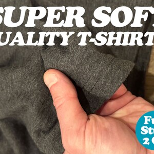 May include: Close-up of a dark gray t-shirt being held in a hand, showing the soft fabric texture. The text "SUPER SOFT QUALITY T-SHIRTS!" is visible at the top of the image. A blue circle with the text "Fun Stuff 2 Go" is visible in the bottom right corner.