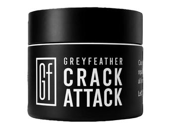 May include: A matte black cylindrical jar with a white screw-top lid. The front label features the white text "GREYFEATHER CRACK ATTACK" and a square logo containing the letters "Gf". The side of the label shows partial white text.