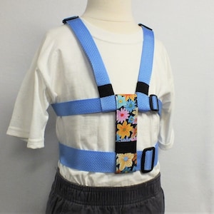 May include: A light blue safety harness with a floral pattern on the chest strap. The harness has adjustable straps and buckles.