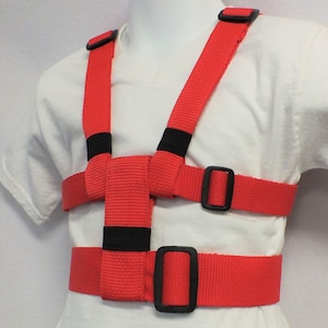May include: Red safety harness with adjustable straps and black buckles. The harness is designed to help keep children safe while walking or running.