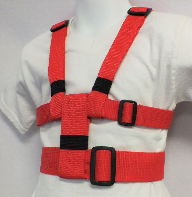 May include: Red safety harness with adjustable straps and black buckles. The harness is designed to help keep children safe while walking or running.