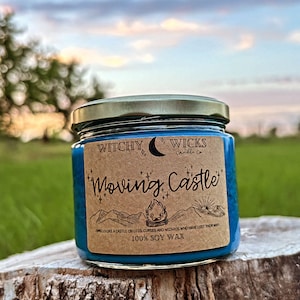 May include: A blue soy wax candle in a glass jar with a gold lid. The label is brown with white text that reads "Witchy Wicks Candle Co. Moving Castle" and "Smells like a castle on legs, curses and wizards who have lost their way. 100% Soy Wax."
