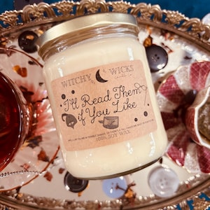 May include: A white soy wax candle in a glass jar with a gold lid. The label is brown with white text that reads "Witchy Wicks Candle Co. I'll Read Them If You Like." The candle is sitting on a gold tray with buttons.