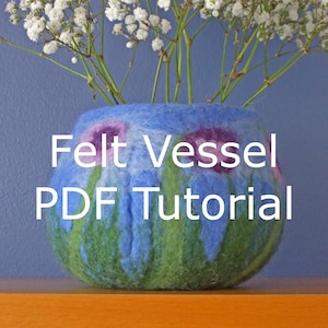 May include: A blue felt vessel with green and purple floral designs. The text "Felt Vessel PDF Tutorial" is printed on the front of the vessel.