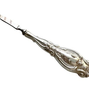May include: A silver nail file with an ornate, detailed handle. The handle is decorated with a floral design.