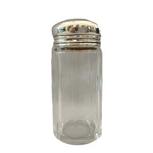 May include: A clear glass jar with a silver lid. The jar has a ribbed design and is empty.