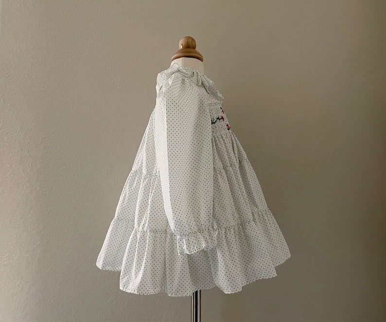 Op de afbeelding: Witte jurk met zwarte stippen en een gerimpelde halslijn. De jurk heeft een smok-lijfje en een gelaagde rok.
