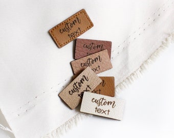 May include: Assortment of small leather labels with the text "custom text" in a handwritten font. The labels are in various shades of brown and beige.