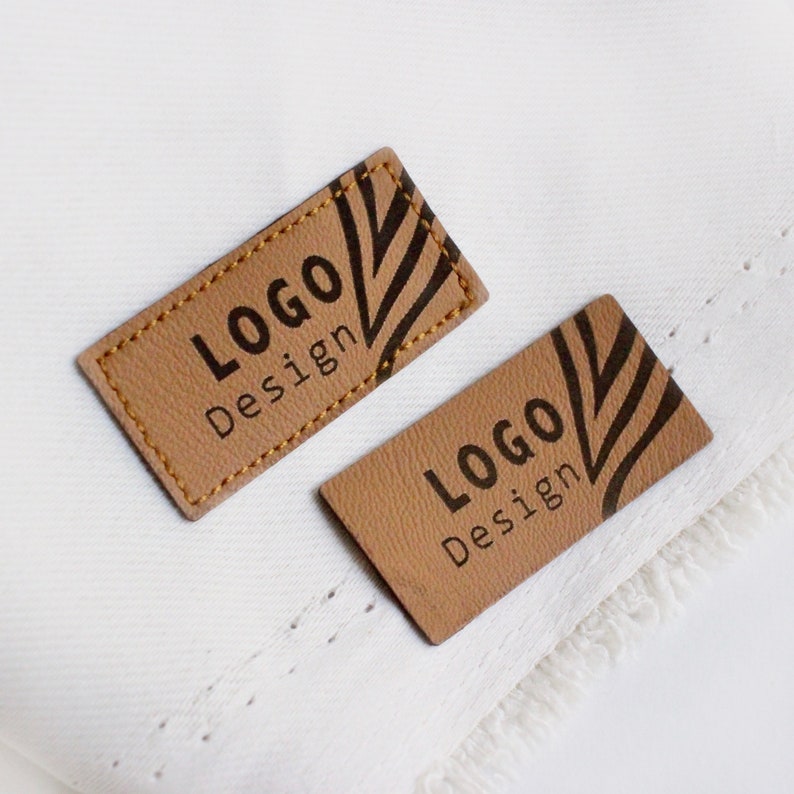 Op de afbeelding: Twee bruine leren labels met een zwart-wit gestreept patroon en de tekst "LOGO Design" erop gedrukt.