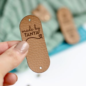 May include: A brown leather tag with holes for string. The tag has the text "made by TANYA" with a heart symbol.