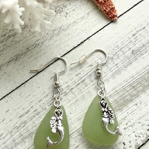 May include: A pair of earrings with green sea glass teardrop dangles and silver mermaid charms.