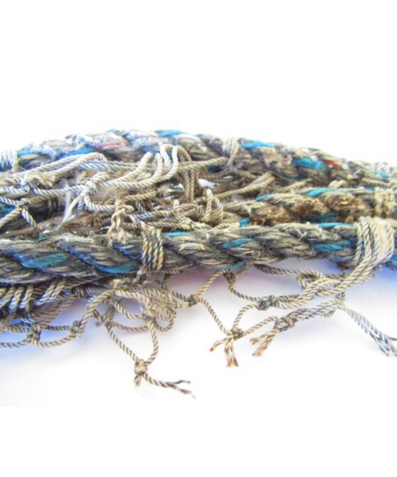Puede incluir: Primer plano de un mont&oacute;n enredado de cuerda gruesa de color gris con detalles azules. La cuerda est&aacute; deshilachada y desgastada, con extremos sueltos que cuelgan.