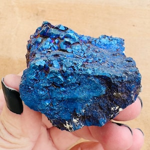 May include: A large, rough, blue crystal with iridescent shimmer. The crystal has a dark blue color with a metallic sheen.