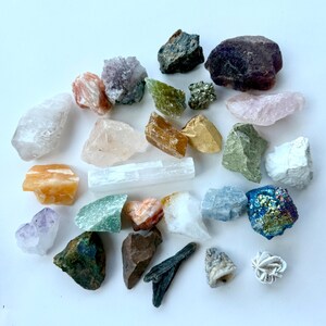 May include: A collection of 25 assorted crystals and stones, including amethyst, rose quartz, selenite, and pyrite. The crystals are arranged on a white background.