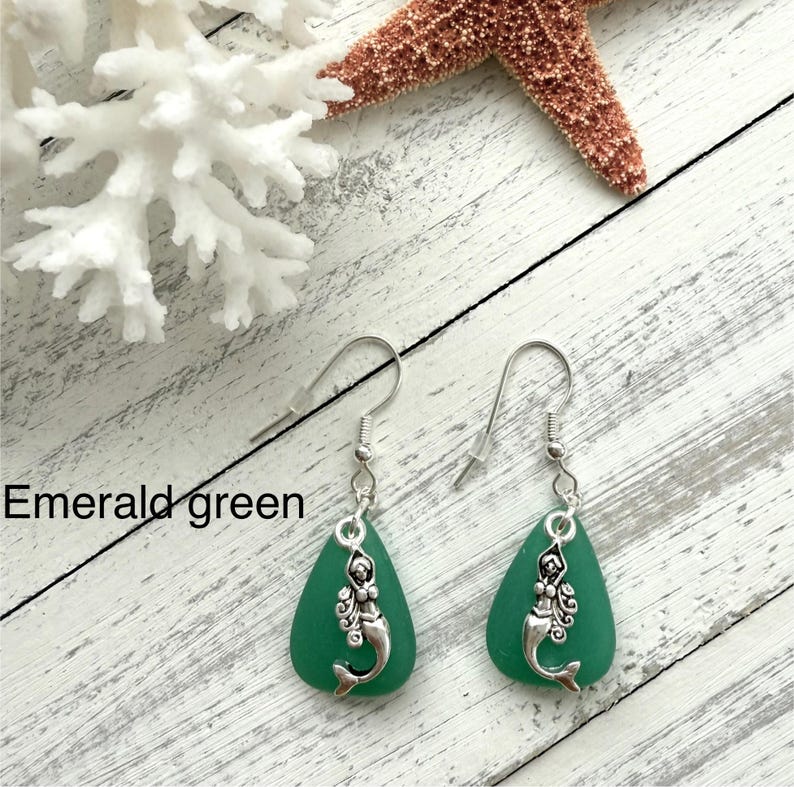 May include: A pair of emerald green sea glass earrings with silver mermaid charms hanging from silver hooks.