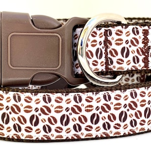 May include: A brown and white dog collar with a coffee bean pattern. The collar has a brown plastic buckle and a silver metal D-ring.
