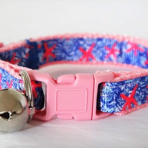 Peut inclure: Collier pour chat rose avec un motif bleu et blanc repr&eacute;sentant des &eacute;toiles de mer rouges. Le collier a une boucle rose et une clochette argent&eacute;e.