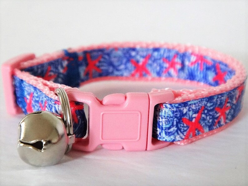 Peut inclure: Collier pour chat rose avec un motif bleu et blanc repr&eacute;sentant des &eacute;toiles de mer rouges. Le collier a une boucle rose et une clochette argent&eacute;e.