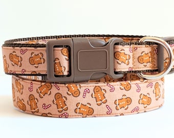 May include: A brown dog collar with a gingerbread man and candy cane pattern. The collar has a brown buckle and a silver D-ring.